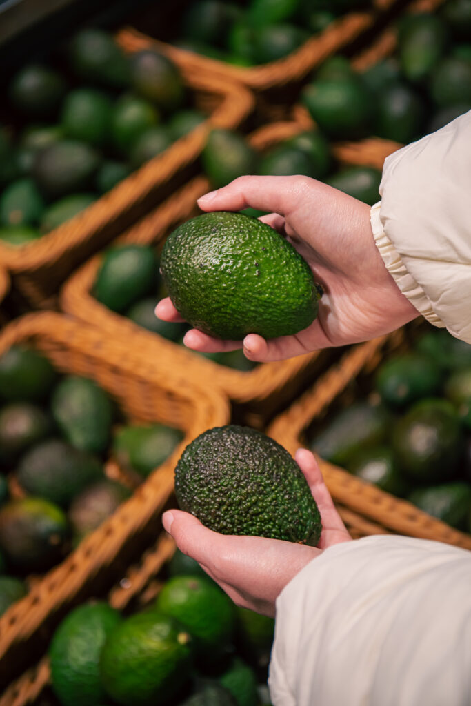 A woman chooses an avocado in a grocery store, close-up, buying organic food for cooking.